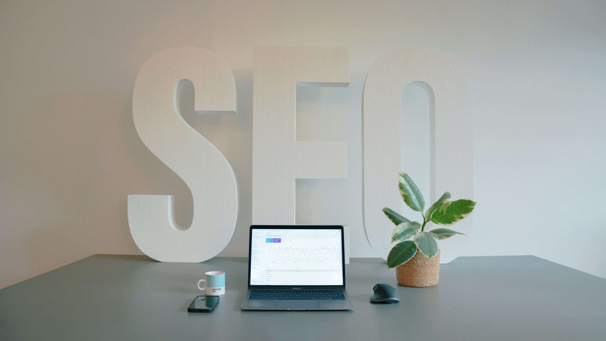 SEO workspace with a laptop displaying analytics and large SEO letters in the background.